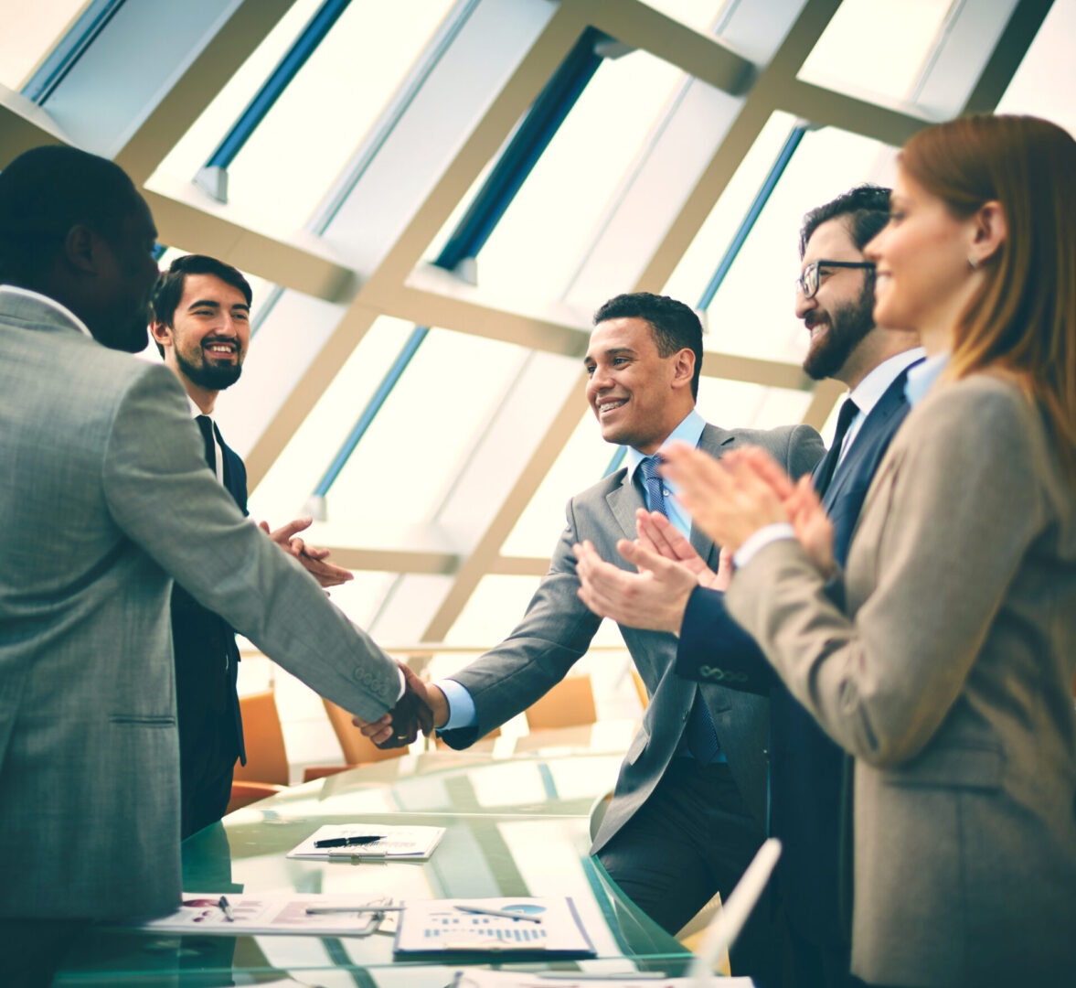 Two successful businessmen handshaking while their colleagues congratulating them